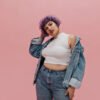 Cool woman with short multi-colored hair in round earrings, white T-shirt, large denim jacket and in light pants looks at camera on pink background. Para look de oficina o salidas